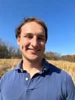 Isaac Chen standing in a prairie wearing a blue polo shirt. A tree line in the background.