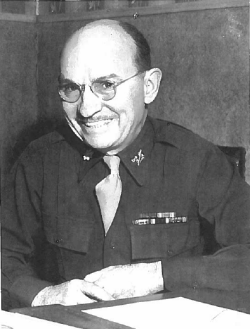 Clair Hamilton sitting at a desk smiling in his Army uniform