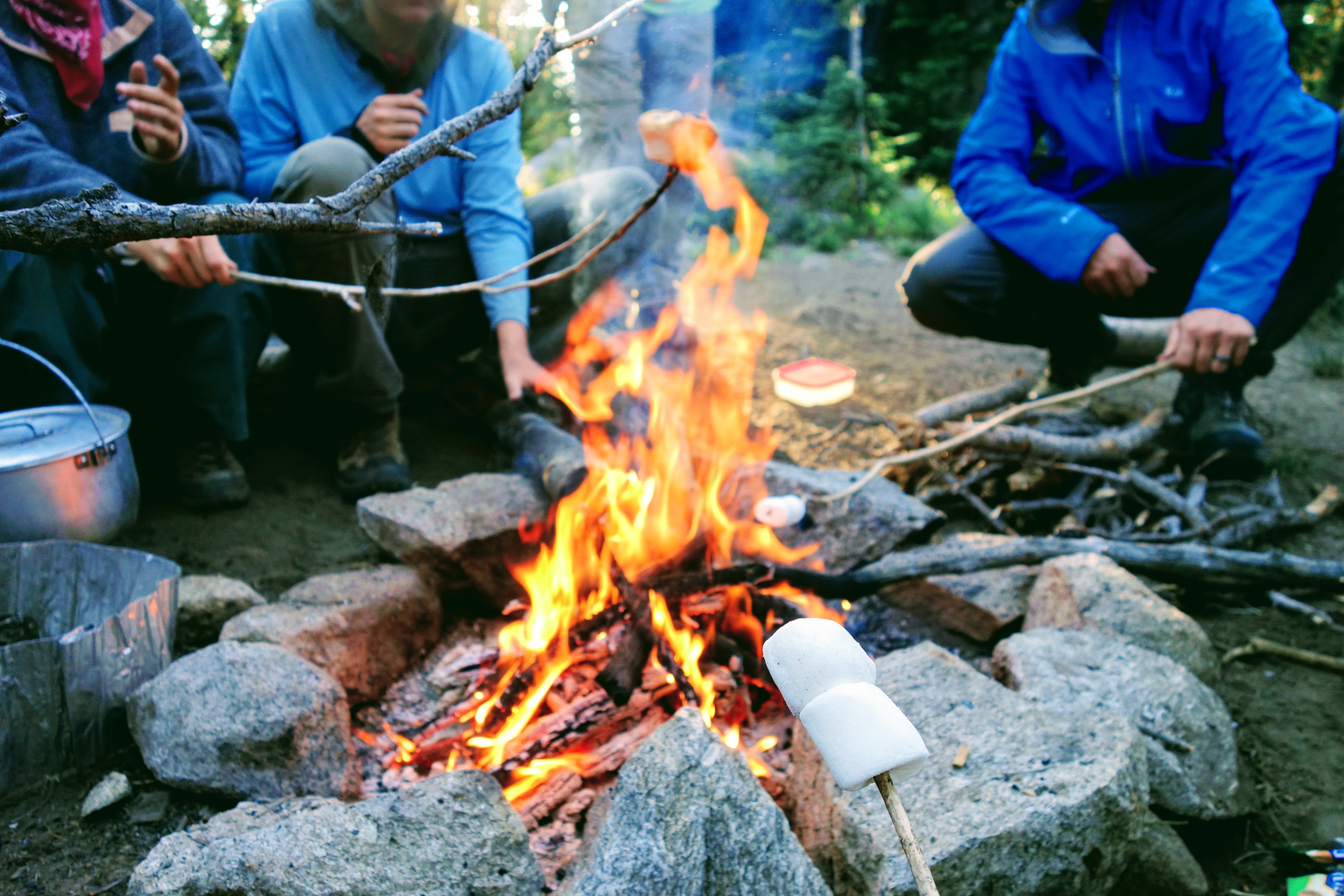 A group of people sit around a fire while roasting marshmallows.