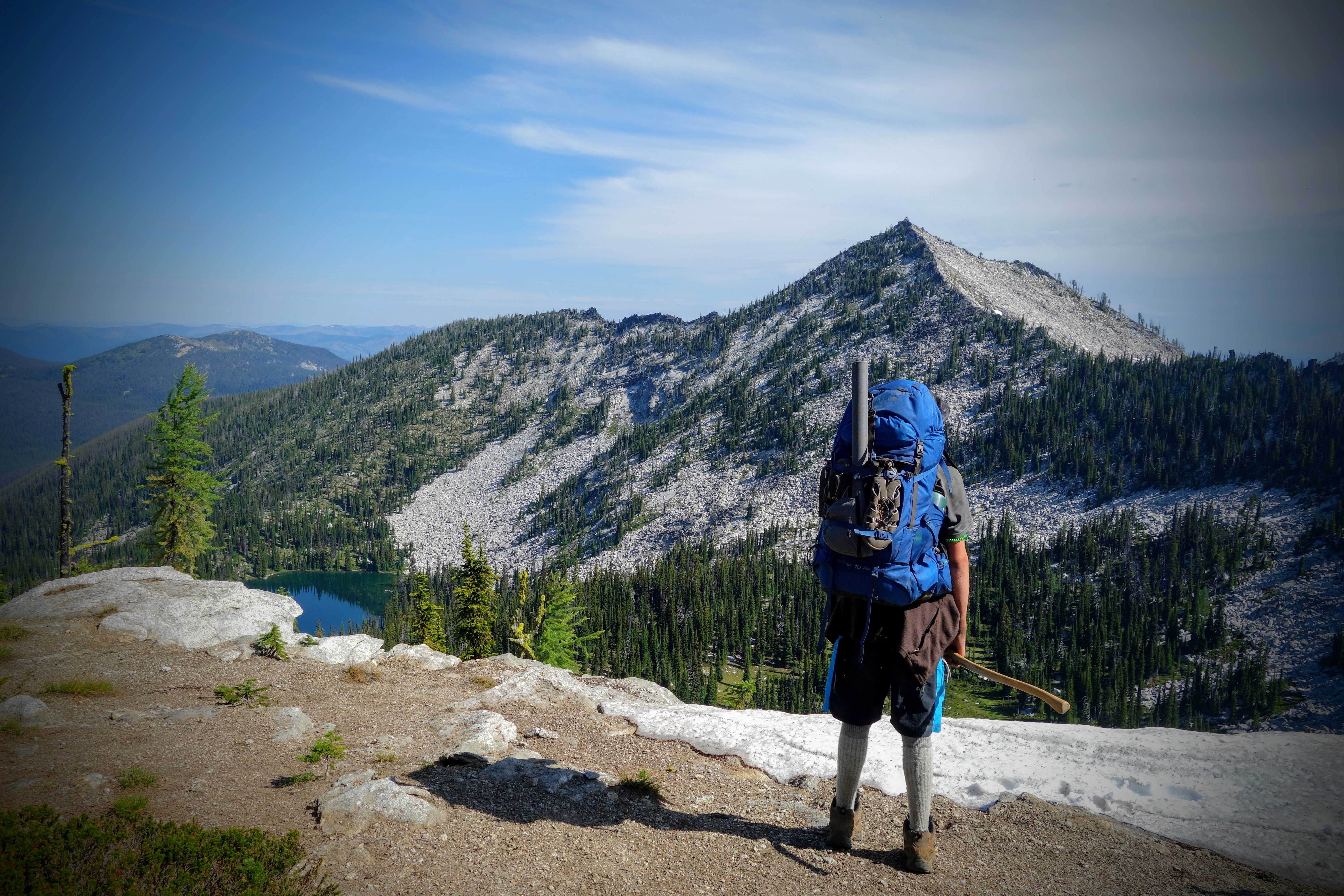 A student with a backpack on stands on the trail facing a mountain vista in the distance.