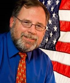 John Mikelson years later smiling in front of the American flag