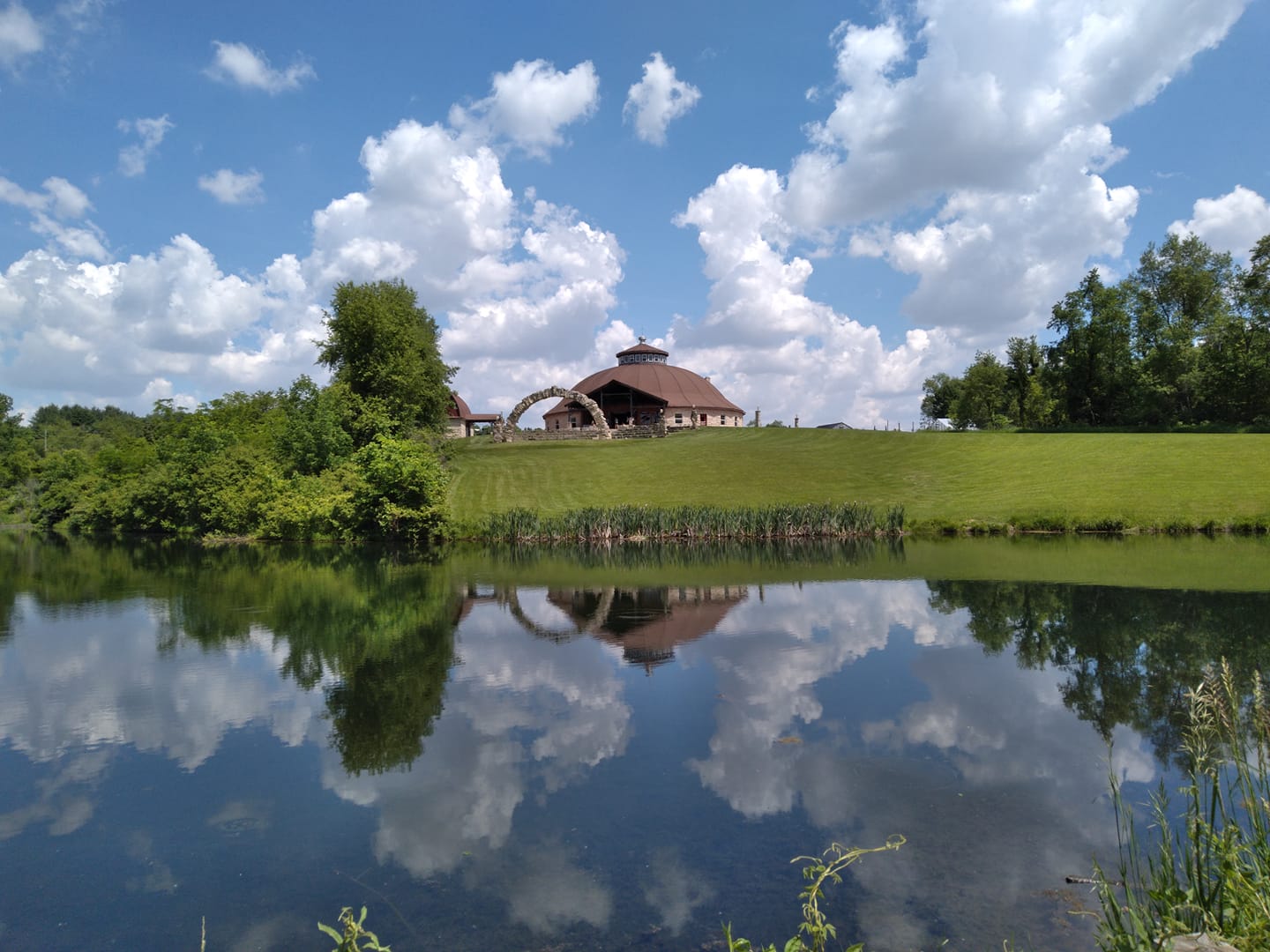 Cangleska Wakan Celebration Barn view from the pond looking up toward the arch and the round barn.