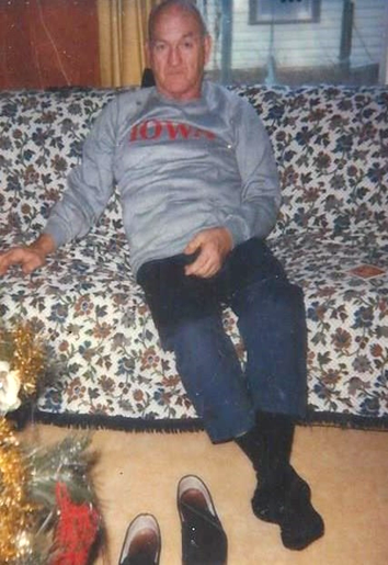 Roy Foens sitting on a couch wearing a Iowa sweatshirt years after the war