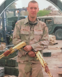 Thomas Webber standing in his Army camp with 2 rifles crossed facing the ground