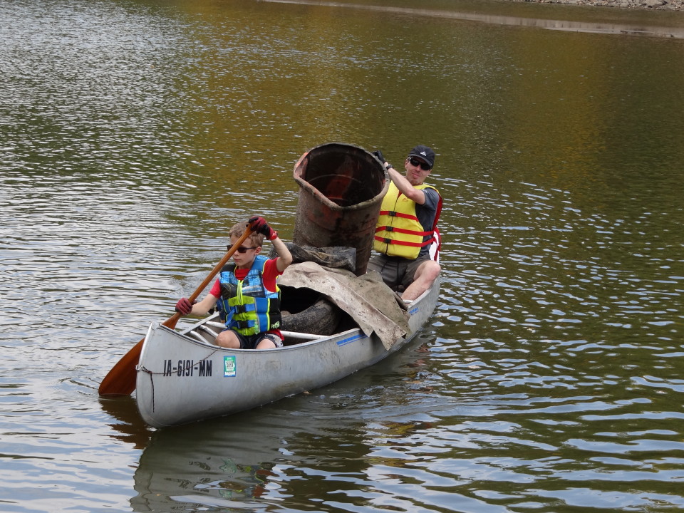 A dad and son paddle a canoe that is loaded with trash removed from the river.